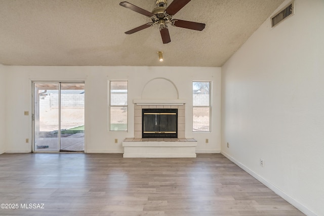 unfurnished living room with vaulted ceiling, a textured ceiling, a fireplace, and light hardwood / wood-style flooring