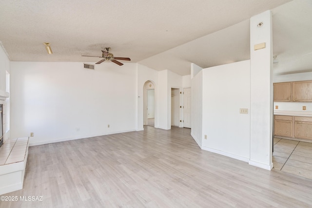 unfurnished living room with vaulted ceiling, ceiling fan, light hardwood / wood-style floors, and a textured ceiling