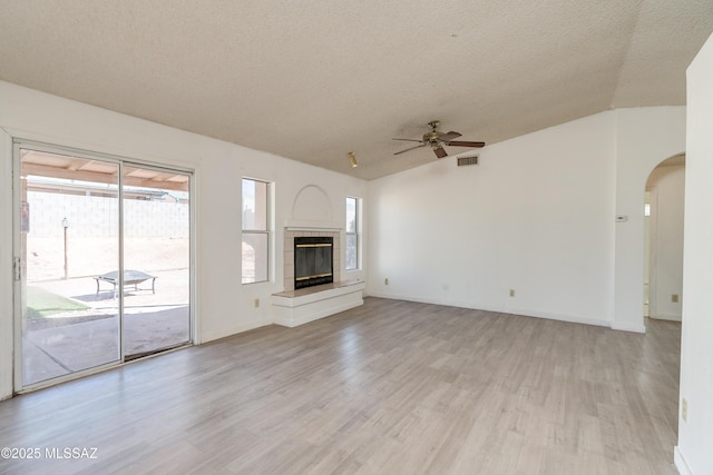 unfurnished living room with vaulted ceiling, a textured ceiling, ceiling fan, a tiled fireplace, and light hardwood / wood-style floors