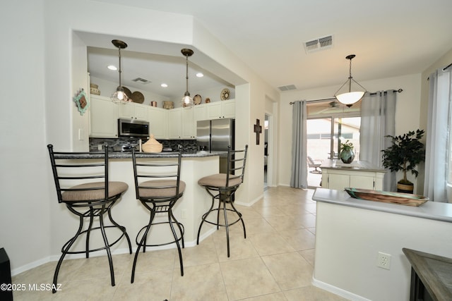 kitchen with white cabinetry, appliances with stainless steel finishes, backsplash, and decorative light fixtures