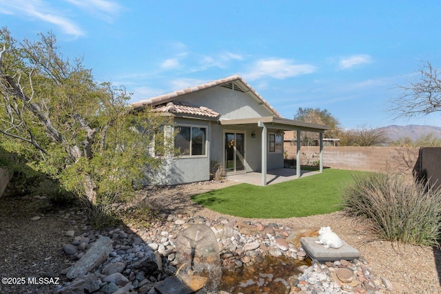 rear view of property featuring fence, a tile roof, a yard, stucco siding, and a patio area