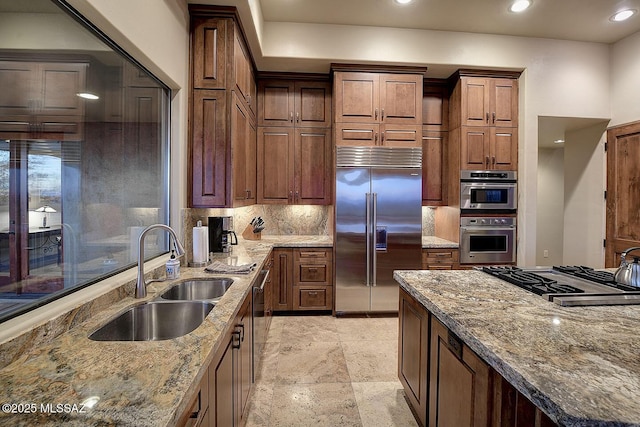 kitchen featuring stainless steel appliances, light stone countertops, sink, and backsplash