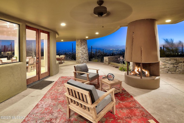 patio terrace at dusk with french doors, ceiling fan, and a multi sided fireplace