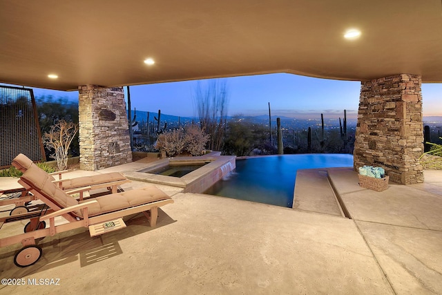 pool at dusk with an in ground hot tub and a patio