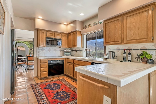 kitchen featuring a sink, decorative backsplash, black appliances, and tile countertops