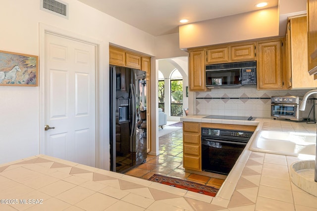 kitchen with tasteful backsplash, arched walkways, visible vents, black appliances, and tile counters