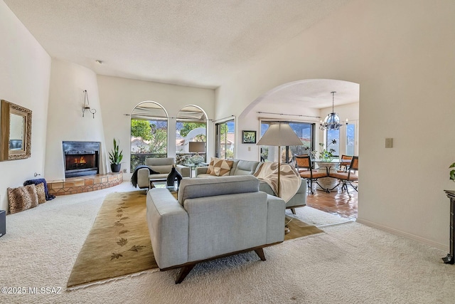 living area featuring an inviting chandelier, carpet, arched walkways, a textured ceiling, and a large fireplace