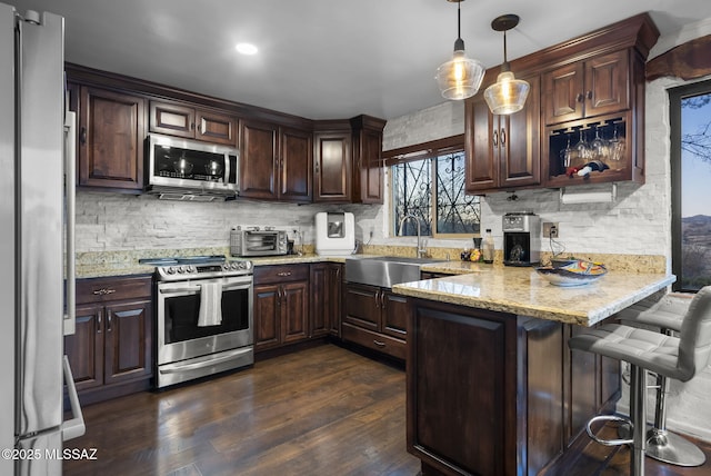 kitchen featuring appliances with stainless steel finishes, decorative light fixtures, sink, kitchen peninsula, and dark brown cabinets