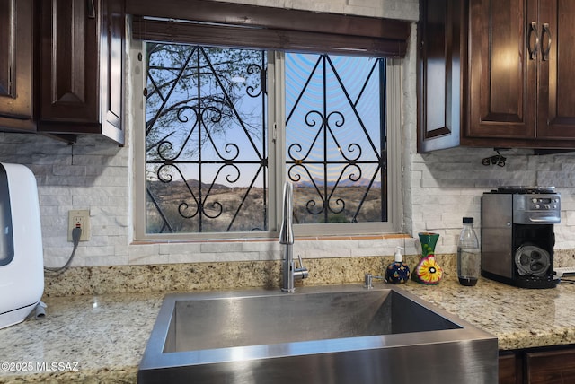 kitchen with tasteful backsplash, light stone counters, sink, and dark brown cabinets