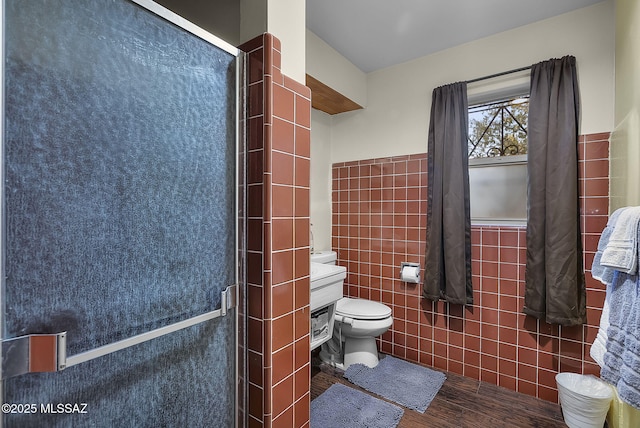 bathroom featuring tile walls, hardwood / wood-style floors, a shower with door, and toilet