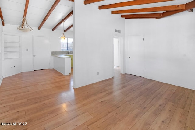 empty room featuring vaulted ceiling with beams, sink, and light wood-type flooring