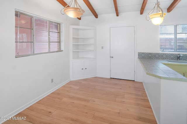 unfurnished dining area with sink, beam ceiling, and light hardwood / wood-style floors