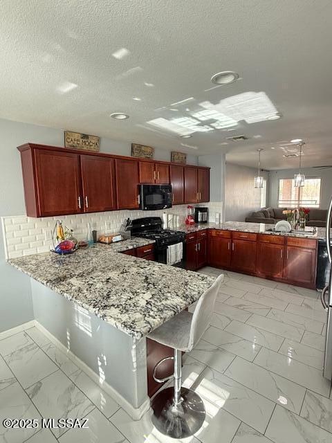 kitchen with decorative light fixtures, kitchen peninsula, light stone countertops, and black appliances