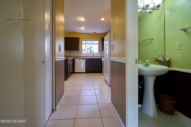 kitchen featuring a sink, stainless steel dishwasher, freestanding refrigerator, light tile patterned flooring, and light countertops