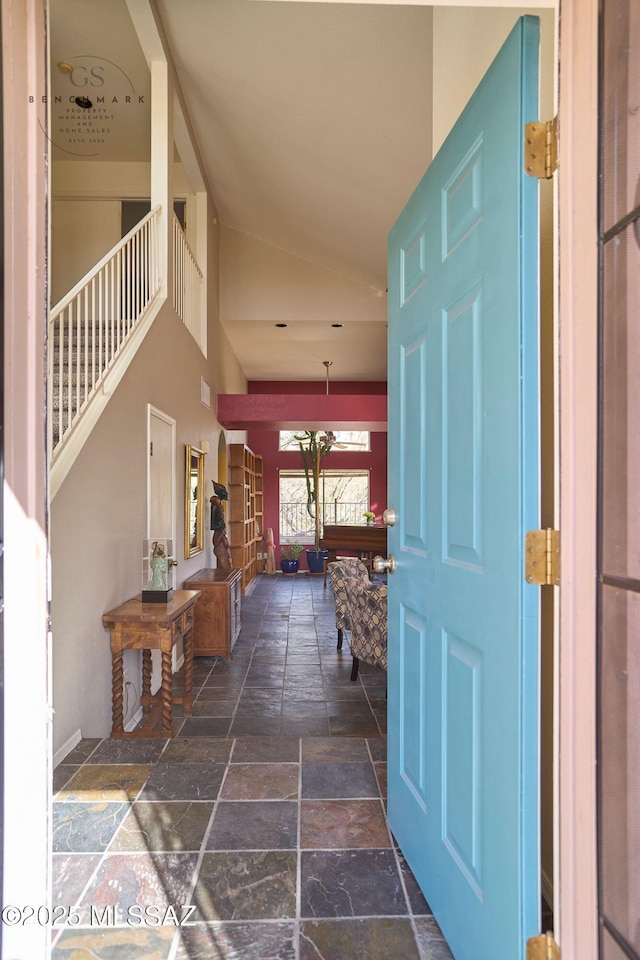 foyer with high vaulted ceiling, stone tile floors, and stairs