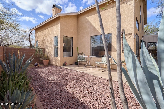 rear view of house with a chimney, a patio area, fence, and stucco siding