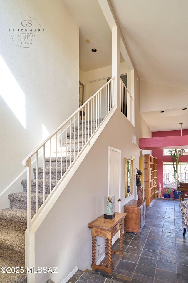 stairs with a high ceiling, visible vents, and stone finish flooring