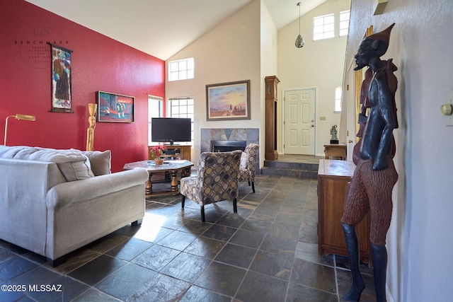 living area featuring high vaulted ceiling, stone tile flooring, and a tiled fireplace