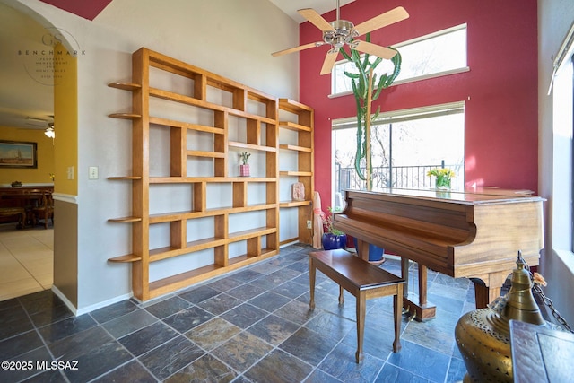 living area with a high ceiling, a ceiling fan, baseboards, and stone finish flooring