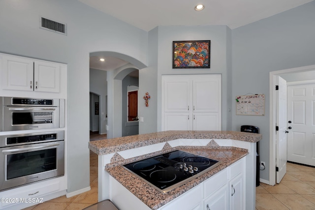 kitchen featuring black electric stovetop, double oven, a kitchen island, and white cabinets