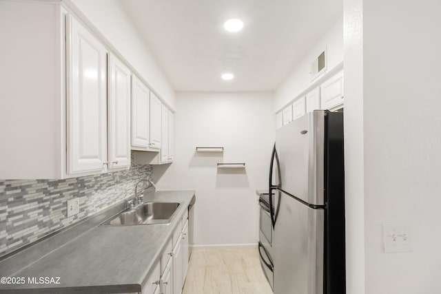 kitchen featuring sink, stainless steel fridge, white cabinetry, backsplash, and range with electric cooktop