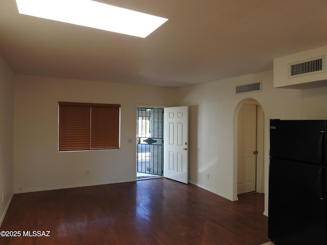 spare room featuring arched walkways, visible vents, baseboards, and wood finished floors