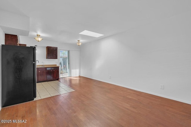 kitchen featuring light wood finished floors, baseboards, light countertops, a skylight, and freestanding refrigerator