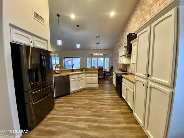 kitchen with pendant lighting, sink, black appliances, wall chimney range hood, and light wood-type flooring