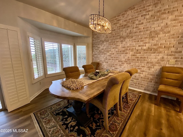 dining area with brick wall, an inviting chandelier, and dark hardwood / wood-style flooring