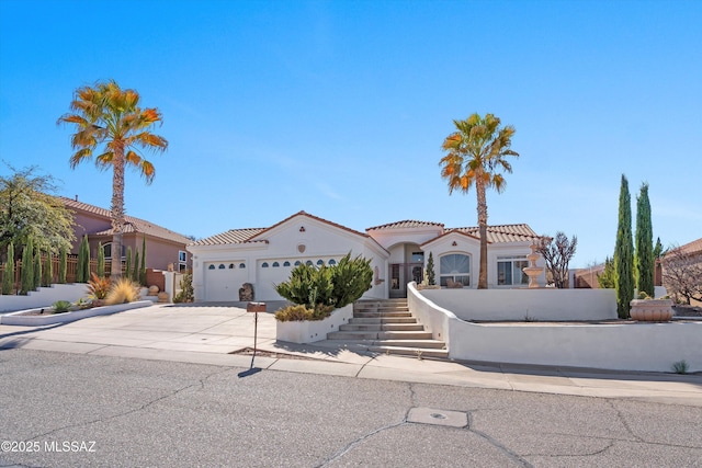 mediterranean / spanish home featuring a tile roof, stucco siding, stairway, a garage, and driveway