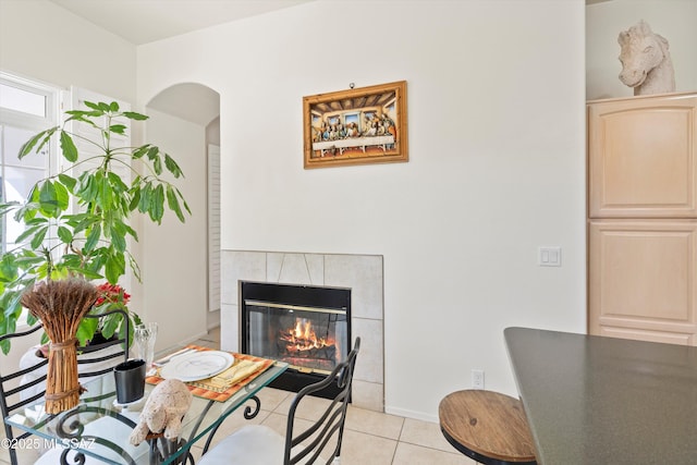 interior space featuring light tile patterned floors, baseboards, arched walkways, and a tiled fireplace
