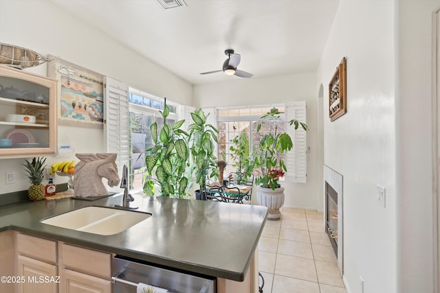 kitchen featuring dishwasher, dark countertops, glass insert cabinets, a fireplace, and a sink