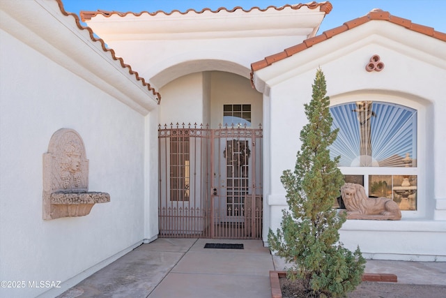 doorway to property featuring a tile roof, a gate, and stucco siding