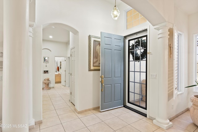 foyer with arched walkways, ornate columns, baseboards, and light tile patterned floors