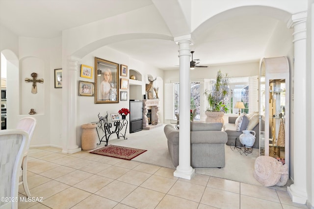 foyer entrance with a ceiling fan, a fireplace, decorative columns, and light tile patterned floors