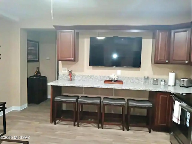 kitchen with electric range oven, a kitchen bar, light stone counters, dark brown cabinets, and light hardwood / wood-style flooring