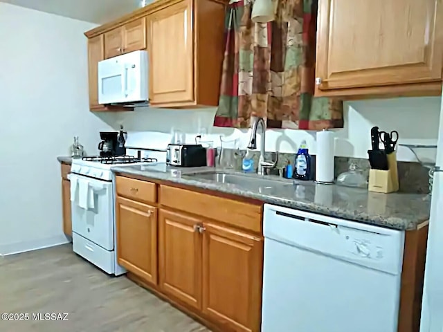 kitchen featuring sink, white appliances, and dark stone counters