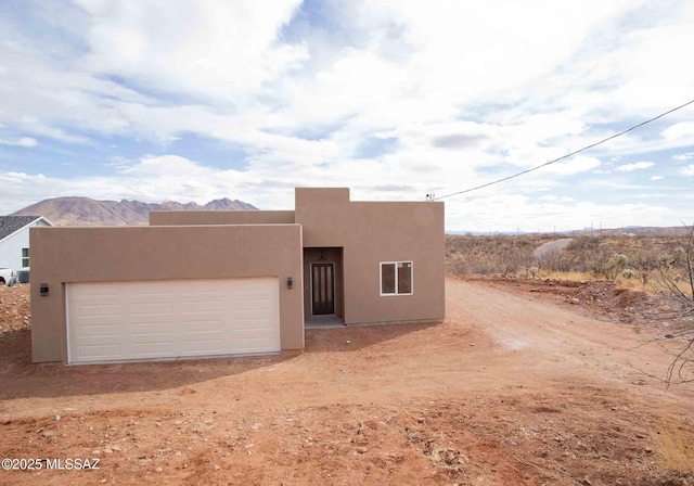 pueblo-style home with stucco siding, an attached garage, a mountain view, and dirt driveway