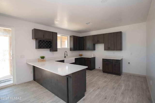 kitchen featuring a peninsula, dark brown cabinetry, light countertops, and light wood-style flooring