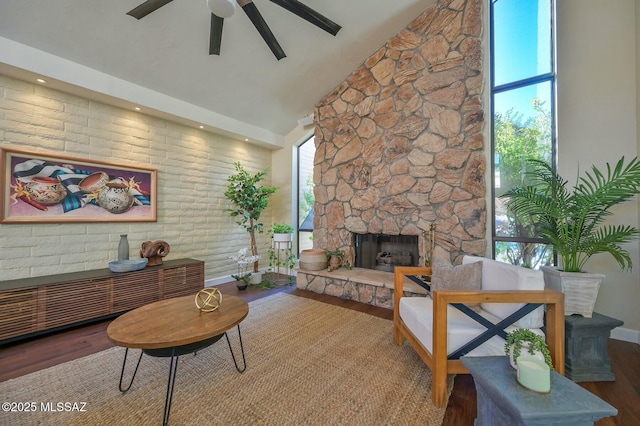 living room with hardwood / wood-style flooring, ceiling fan, a stone fireplace, and high vaulted ceiling