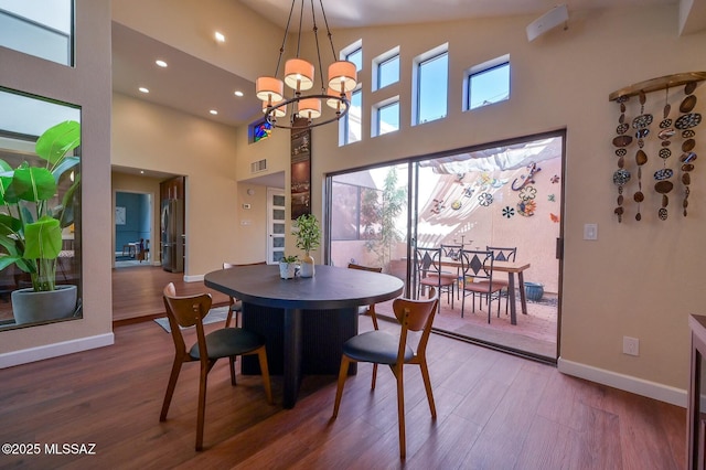 dining space featuring wood-type flooring, a towering ceiling, and a chandelier