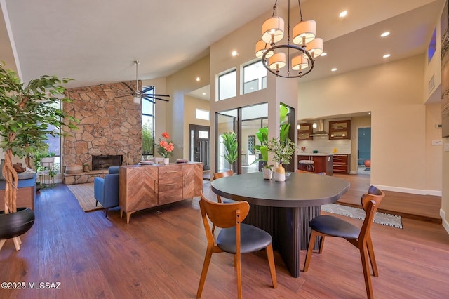 dining room with a fireplace, a towering ceiling, dark wood-type flooring, and ceiling fan with notable chandelier