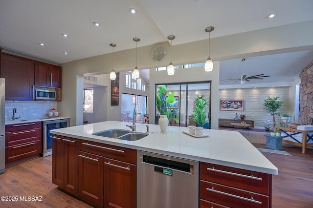 kitchen featuring sink, hanging light fixtures, a center island with sink, stainless steel appliances, and beverage cooler