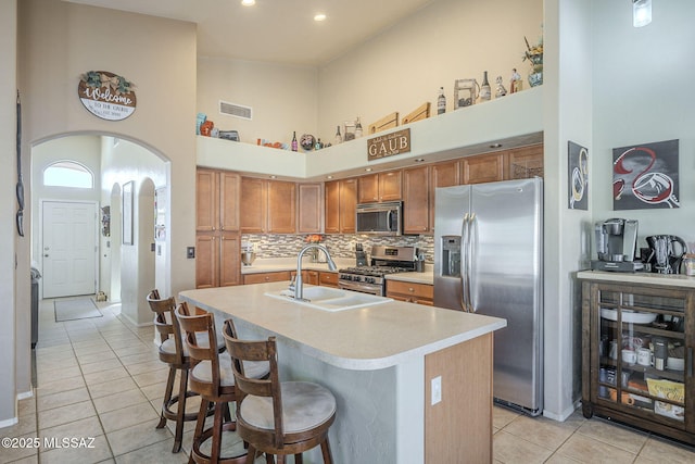 kitchen with a center island with sink, arched walkways, stainless steel appliances, light countertops, and a sink