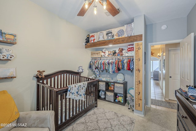 bedroom featuring a crib, a closet, a ceiling fan, and light colored carpet