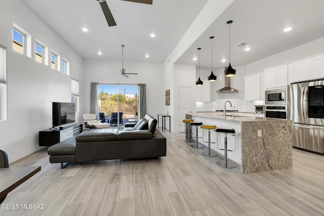 living area featuring light wood-style floors, visible vents, a towering ceiling, and a ceiling fan