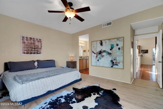 bedroom featuring ceiling fan, ensuite bath, and light wood-type flooring