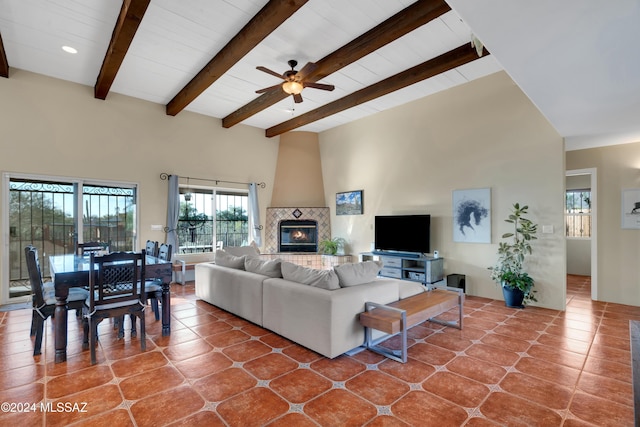 living room with ceiling fan, a towering ceiling, a tiled fireplace, tile patterned floors, and beamed ceiling