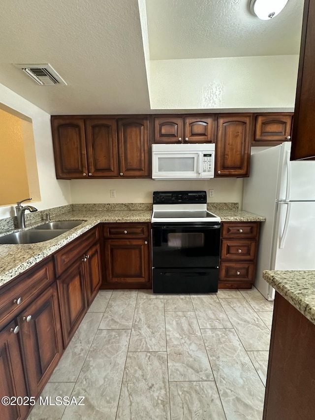 kitchen featuring visible vents, a sink, a textured ceiling, light stone countertops, and white appliances