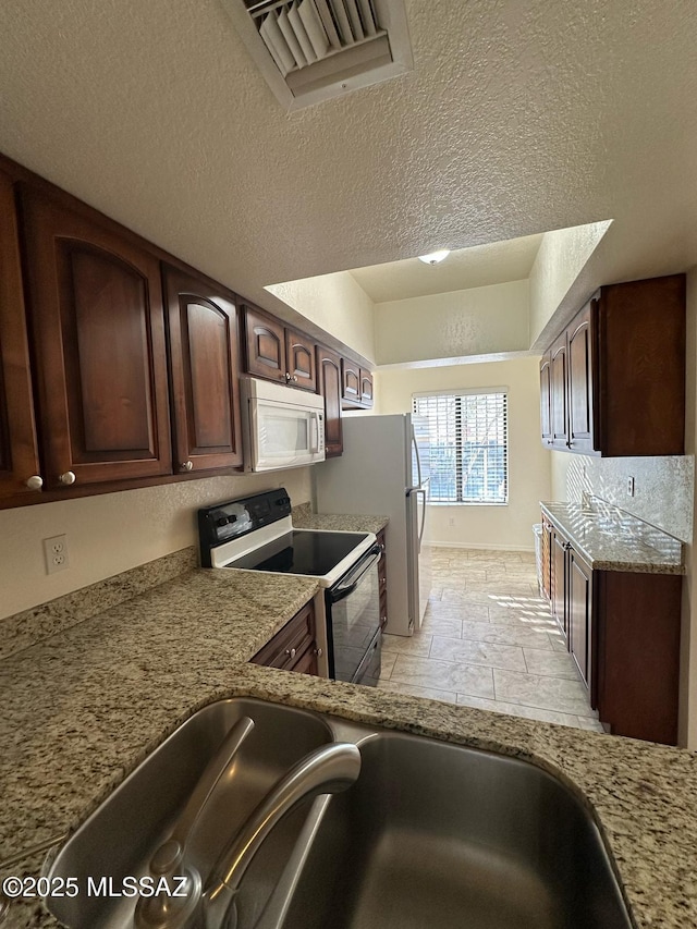 kitchen with dark brown cabinetry, white appliances, visible vents, light stone countertops, and a sink